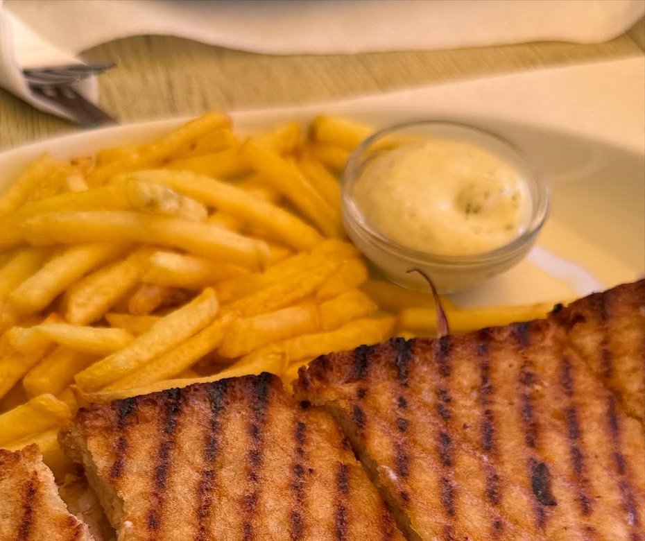 Tosta grelhada cortada em triângulos, com batata frita e uma taça de molho