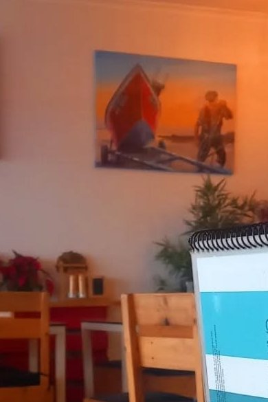 Sala com cadeiras de madeira, um quadro com um barco de pesca e a carta de bebidas em primeiro plano